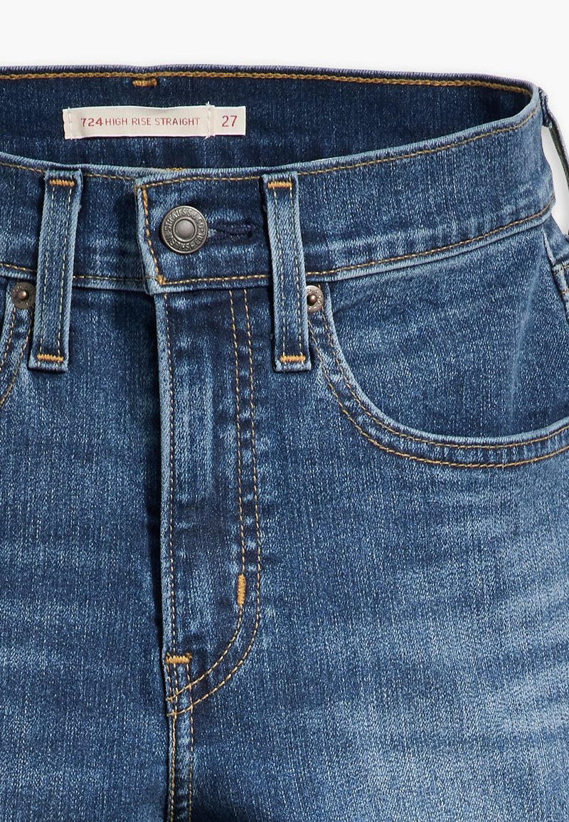 Jean droit taille haute en denim bleu, avec des coutures visibles, une fermeture à bouton et des poches avant. L'étiquette de taille indique 27.