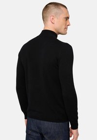 Schwarzer Strickpullover mit hohem Kragen, schmaler Passform und langen Ärmeln; getragen mit dunklen Jeans; glatte Textur; minimales Design ohne Verzierungen.