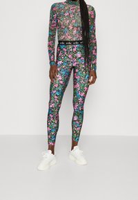 Blomsterprint langærmet top og leggings i sort med pink, blå og grønne blomster. Blødt stof med en tætsiddende pasform og elastisk talje. Hvide sneakers.