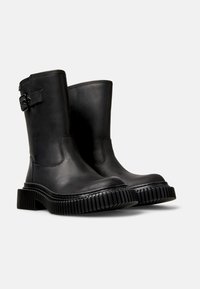 Black leather ankle boots with a round toe, featuring a side strap with a buckle, and a thick, ribbed rubber sole for traction.
