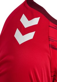 Röd atletisk tröja med rund hals, med en strukturerad yta och djärva vita chevron-mönster på axeln.