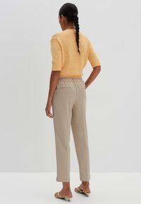 Oranges Strickpullover mit kurzen Ärmeln, kombiniert mit beigen Hosen mit elastischem Bund und seitlichen Taschen, von hinten betrachtet.