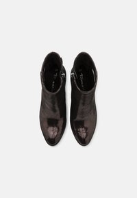 Paire de bottines noires brillantes avec fermetures éclair latérales, vues de dessus sur fond blanc uni.