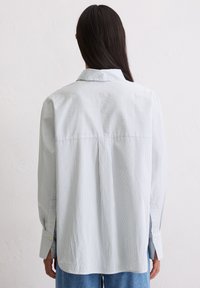 Világoskék csíkos ing laza szabással, hosszú ujjal és klasszikus gallérral. Hátul yakkal és gombos mandzsettával díszített.