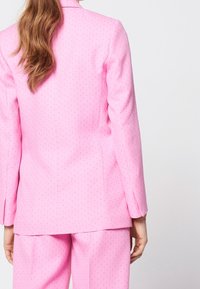 Completo rosa con giacca aderente e pantaloni abbinati. Il tessuto presenta un leggero motivo testurizzato e una finitura liscia.