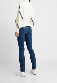 Bílý pletený svetr s černými kostkovanými akcenty, kombinovaný s modrými skinny džíny a bílými teniskami. Minimalistický design, přiléhavý střih.