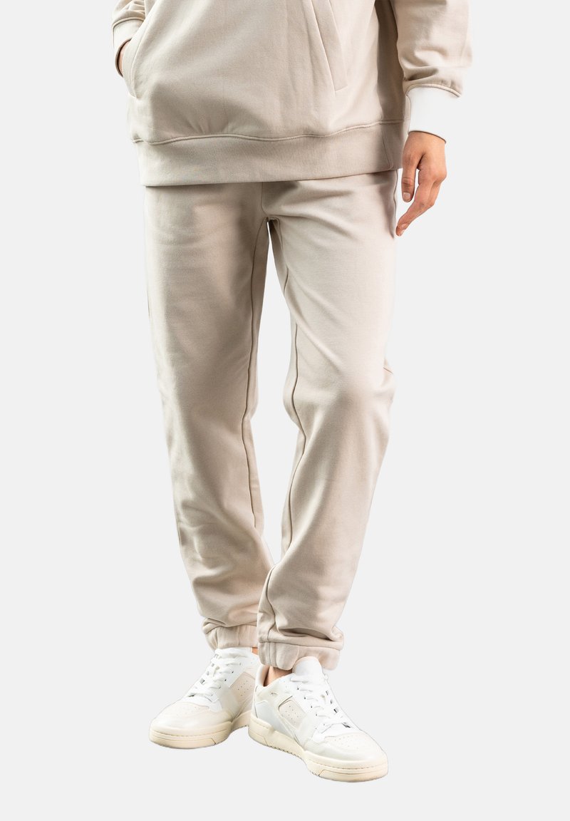 Beige bomulds sweatpants med elastiske manchetter og sidelommer, parret med hvide høje sneakers med perforerede detaljer.