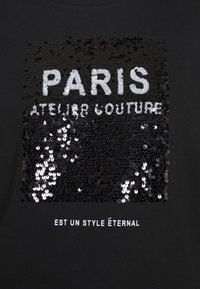 Sudadera negra con un diseño de cuadrado con lentejuelas que lleva el texto "PARIS ATELIER COUTURE" en blanco, y "EST UN STYLE ÉTERNAL" debajo.