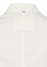 Biała koszula z klasycznym kołnierzykiem, z pionowym szwem i małą prostokątną naszywką. Gładka tekstura, minimalistyczny design, subtelne przeszycia.