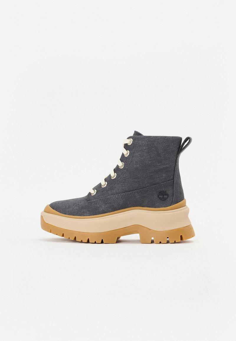 Botas de tornozelo em denim com uma sola grossa bege, atacadores creme e um laço atrás. Detalhe do logotipo na lateral.