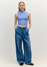 Lichtblauw geribbeld crop top met hoge halslijn, gecombineerd met loszittende blauwe denim wijde broek en zwarte platform schoenen.