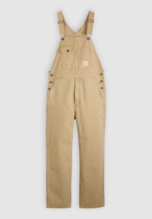 Tuta da lavoro beige con bretelle regolabili, tasche anteriori sul petto, incluso taschino con patta e bottone, bottoni sui fianchi e gambe dritte.