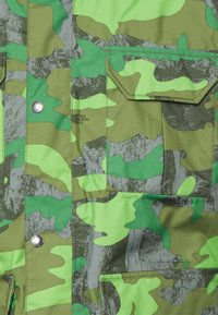 Camo jacket in shades of green with a texture of smooth, synthetic material. Features multiple pockets and silver snap buttons.