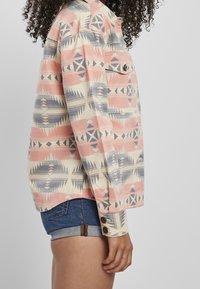 Button-up skjorte med et multi-farvet geometrisk mønster i pink, beige og blå, lavet af et letvægtsstof; lomme detalje synlig.