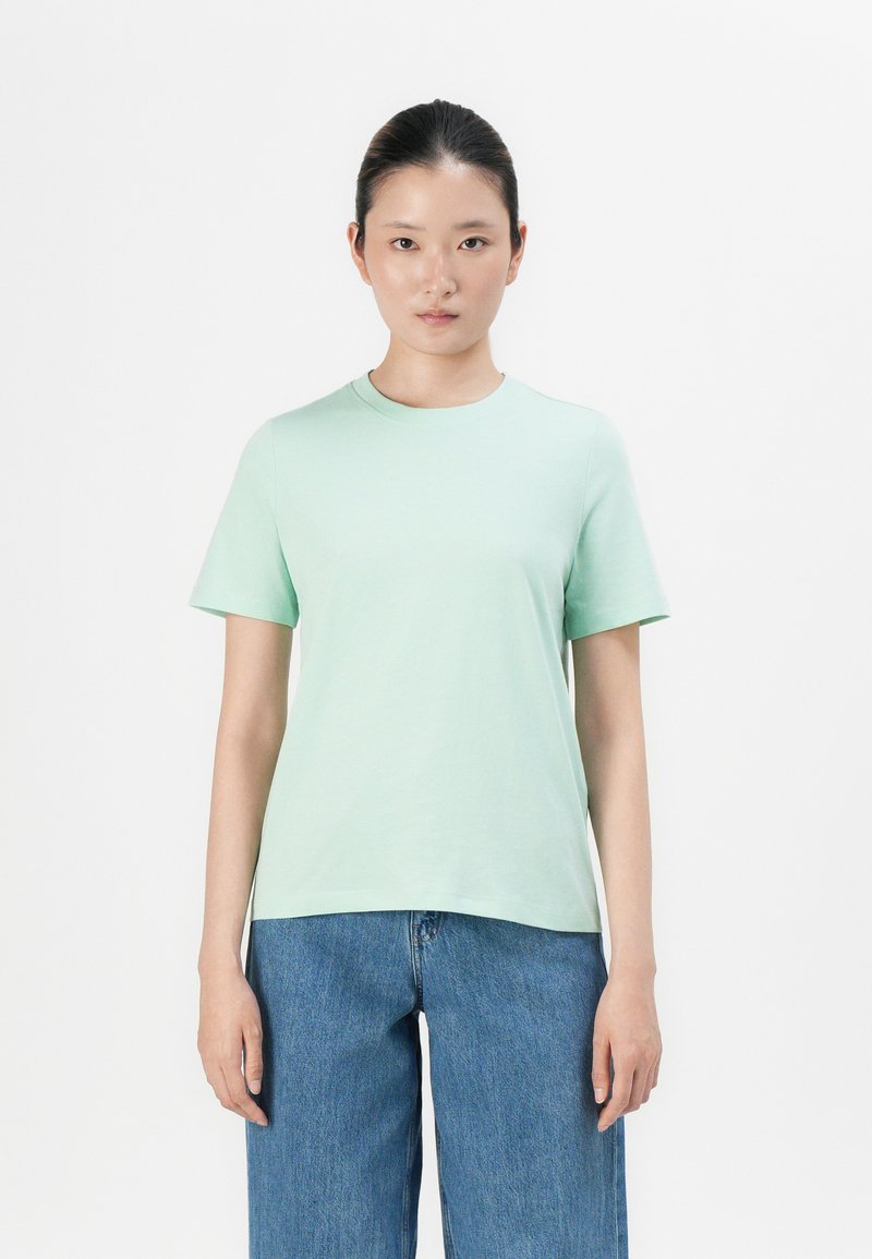 Mintgrön bomulls-T-shirt med kort ärm, rund halsringning och avslappnad passform, kombinerad med ljusblå vida denimjeans.