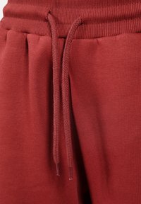 Czerwone dresy z teksturowanej tkaniny, z elastycznym pasem i sznurkiem z plecionką. Zawierają fałdy z przodu dla zwiększenia objętości.