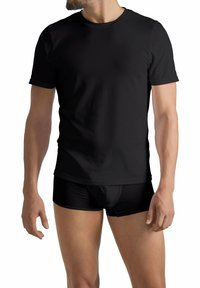 Uomo che indossa una semplice maglietta nera a maniche corte e boxer neri, in piedi su uno sfondo bianco.