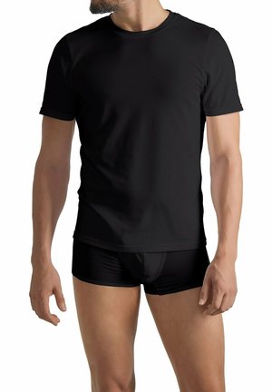 Hombre vistiendo una camiseta negra de manga corta y unos bóxers negros, de pie frente a un fondo blanco.