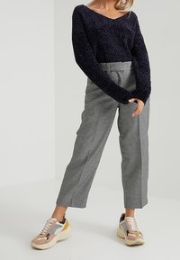 Granatowy sweter na drutach z dekoltem w serek, szerokie rękawy, czarno-białe, wysokie w talii spodnie w kratę oraz wielokolorowe, masywne sneakersy.