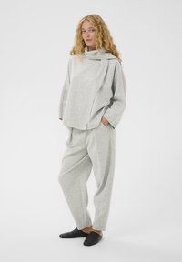 Világosszürke, túlnyúló pulóver szett, hosszú ujjú felsővel, állógallérral és redőzéssel, laza, picit szűkülő nadrággal párosítva.