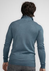 Gehaakte trui in tealblauw met een hoge kraag, ribbelmanchetten en zoom; gladde textuur en aangesloten silhouet.