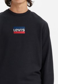 Svart sweatshirt med rund hals, med en rektangulär Levi's-logotyp i rött, vitt och blått över bröstet. Slät textur.