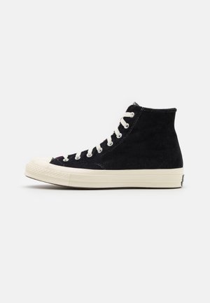 High-top sneakers made of black suede with white laces, cream rubber sole, rounded toe cap, and classic logo on the heel.