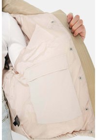Giacca esterna beige con fodera rosa chiaro, chiusura a bottone a pressione e tasca applicata. L'interno presenta una sottile brandizzazione sul tessuto.