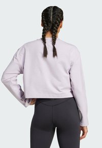 Licht paarse cropped sweatshirt met lange mouwen, gemaakt van zachte stof. Heeft een ronde hals en zijslits. Gecombineerd met zwarte leggings.