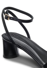 Μαύρο δερμάτινο σανδάλι με τακούνι block και λεπτό λουράκι στον αστράγαλο με μικρή χρυσή αγκράφα.