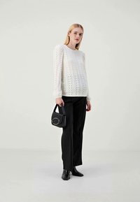White, long-sleeve top with eyelet pattern and gathered cuffs, paired with black wide-leg trousers and a small black handbag.