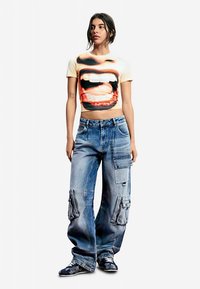 Beige cropped T-shirt met een mondgrafiek, gecombineerd met oversized blauwe denim cargobroeken met meerdere zakken en een vervaagde afwerking.