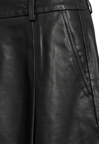 Gonna nera in pelle con una superficie liscia e strutturata, tasca frontale e una cintura elegante. Design sartoriale con linee pulite.