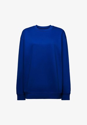 Blaues Sweatshirt mit kariertem Kragen, kombiniert mit einer weißen Hobo-Tasche. Die Tasche hat eine glatte Textur und runde Form und wird von dem Model gehalten.