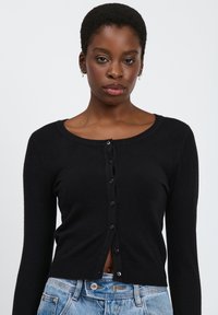 Schwarzer Cardigan aus Strickmaterial mit runder Ausschnittkante, langen Ärmeln und Knopfleiste. Mustervariante und kurze Länge.