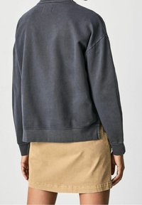 Felpa grigia scura con spalle scese, polsini a costine e un orlo che arriva a metà schiena, abbinata a una mini gonna in denim beige.