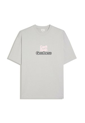 Hellgraues T-Shirt mit kurzen Ärmeln und dem Text "Can't Rush Greatness" in weißem und schwarzem Text auf der Vorderseite in der Mitte bedruckt.