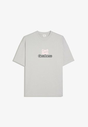 T-shirt grigio chiaro a maniche corte con la frase "Can't Rush Greatness" stampata in bianco e nero al centro davanti.