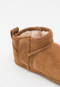 Hnedé semišové kotníkové topánky so soft, vlneným interiérom, zaobleným dizajnom a šitým švom pozdĺž okraja. Obsahuje malú ťahaciu pútko.