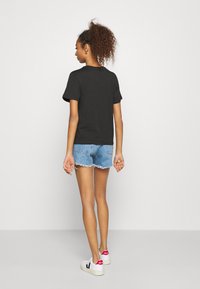 Sort bomuld t-shirt med korte ærmer, parret med slidte denimshorts og hvide sneakers med røde detaljer på hælen.
