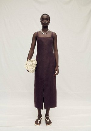 Robe longue sans manches de couleur prune avec un décolleté carré, fente à l'avant, associée à un sac crème avec des accents floraux et des sandales.