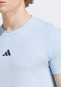 Světle modré tričko s krátkým rukávem vyrobené z lehkého materiálu, které má černé logo Adidas na hrudi a kulatý výstřih.