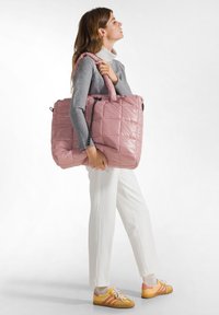 Rosa quiltad tote-väska med en blank yta, som har två handtag och en dragsko-stängning. Väskan är accentuerad med svart metall.