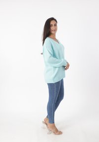 Maglione oversized blu chiaro con scollatura a V, polsini e orlo a coste abbinato a jeans blu aderenti e tacchi trasparenti aperti.