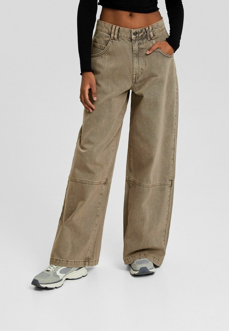 Wide-leg pants in light brown denim, with a high waist, button closure, and side pockets. Paired with gray and white athletic shoes.