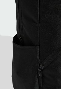 Zaino in tessuto nero con tasca laterale con cerniera, texture liscia, riflesso sottile e cuciture rinforzate lungo le giunture.