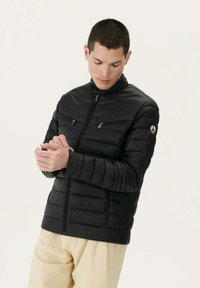 Giacca a vento nera con colletto alto, tasche con zip e design trapuntato. Il materiale è liscio e leggero, adatto per l'uso all'aperto.