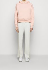 Ljusrosa hoodie med känguruficka och dragsko på huvan, matchad med vita vida byxor och vita sneakers. Slät tygstruktur.