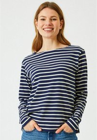 Laivastonsininen ja valkoinen raidallinen pitkähihaisista paita, joka on valmistettu pehmeästä kankaasta, jossa on avara kaula-aukko ja rento leikkaus. Yhdistetty vaaleansinisiin farkkuihin.