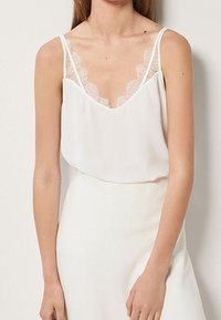 Canotte bianca con rifiniture in pizzo lungo il décolleté e le bretelle, con vestibilità ampia e texture morbida. Progettata con un décolleté a forma di V.